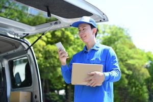 男性配達員がスマートフォンで配送指示を確認する様子（Amazon Flex等の配達アプリを利用した稼働イメージ）